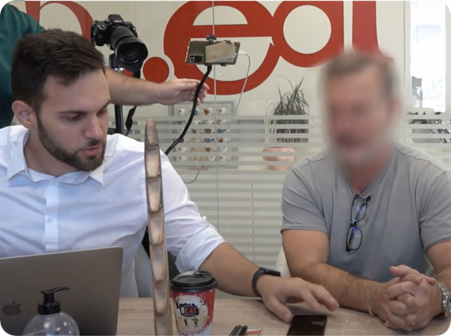 A moderator taking notes beside a participant during a recorded session, with a phone mounted on a rig and a camera on a tripod