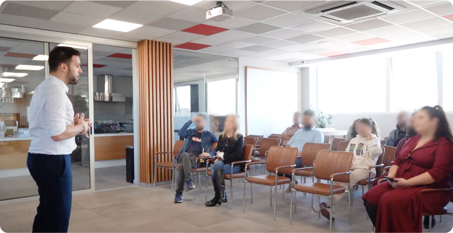 A presenter standing in front of a seated group in an office during a testing session, with participants' faces blurred for privacy